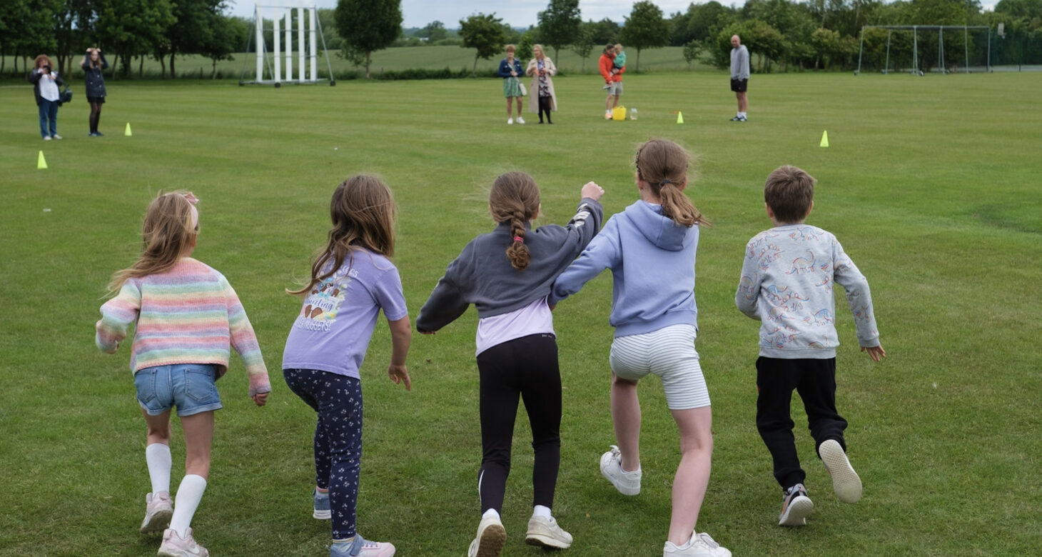 Five children are holding hands and running across a field with their backs to the camera.